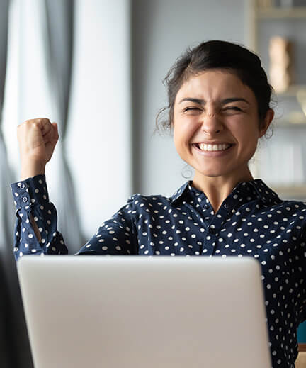woman sitting in front of her computer with her fist in the air, looking triumphant